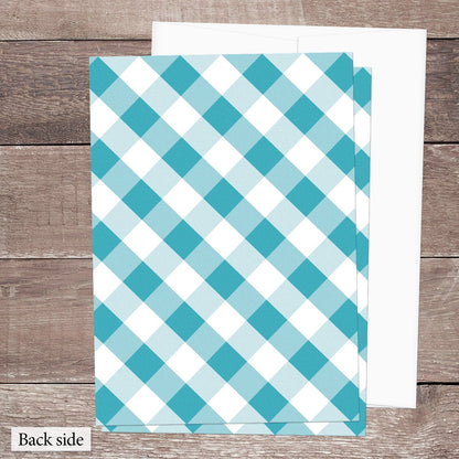 The back side of the Turquoise Gingham Vow Renewal Invitation shown on a brown wood surface with a white envelope.