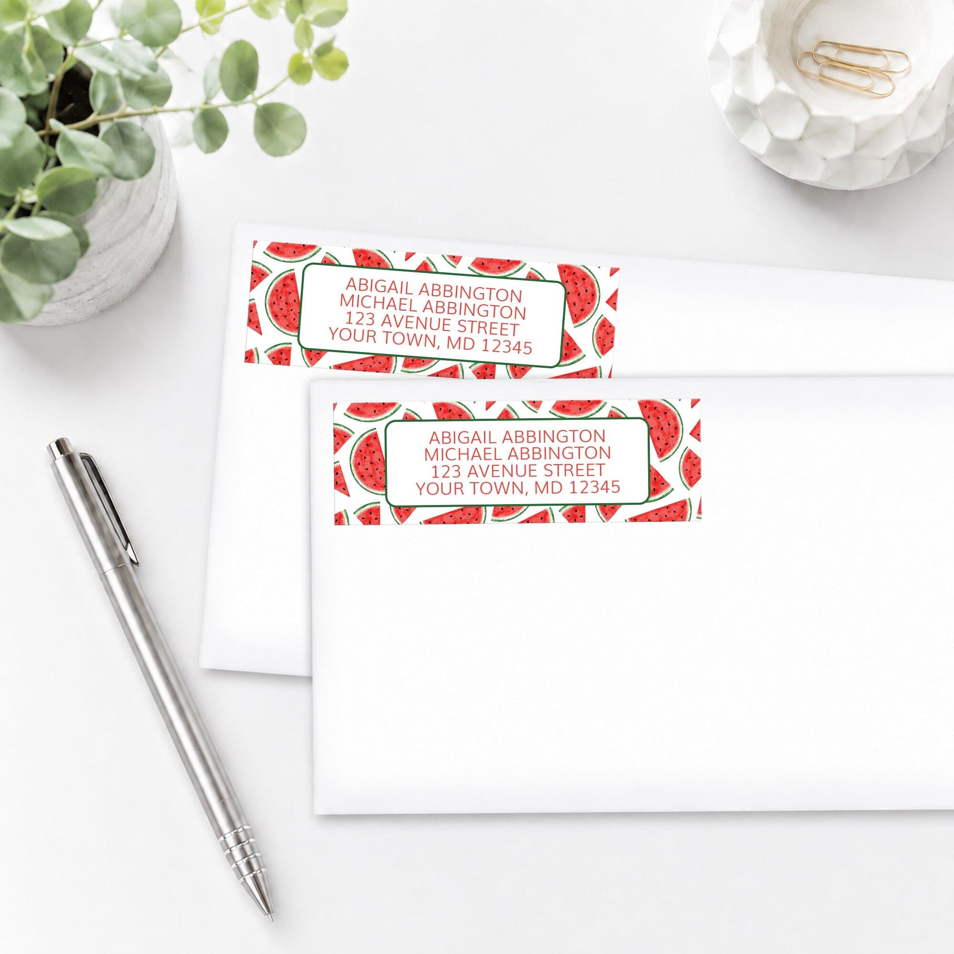 Watermelon Slices Address Labels with watermelon pattern, shown on white envelopes, on a white surface with a pen and plant.