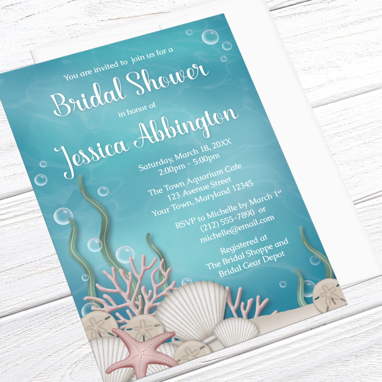 Bridal Shower invitation with an under the sea theme, featuring an underwater illustration, displayed at an angle with a white envelope on a white wood surface