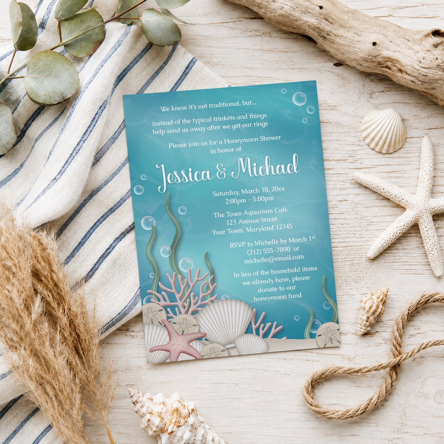 Whimsical Under the Sea Honeymoon Shower Invitation shown on a light wood surface with seashells and coastal decor.