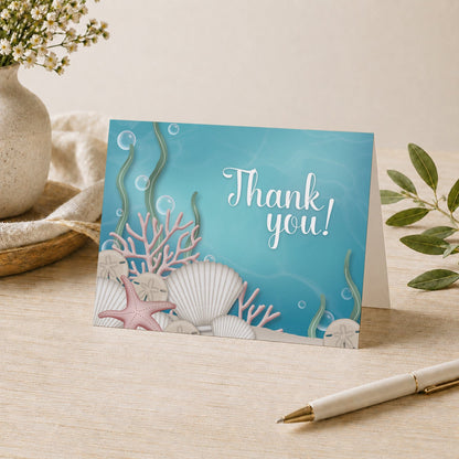 Whimsical Under the Sea Thank You Card shown on a tabletop with a vase, plants, and a pen.