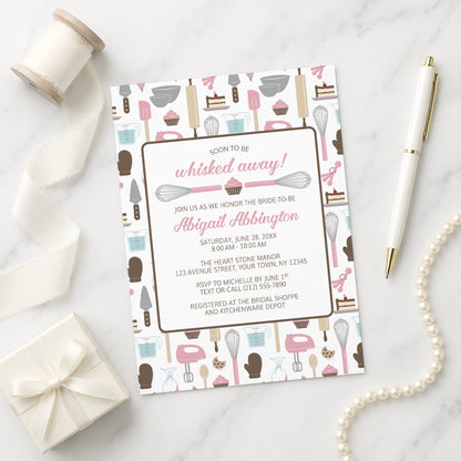 Whisked Away Pink Baking Bridal Shower Invitation with kitchen-themed pattern on a marble surface with decorative items.