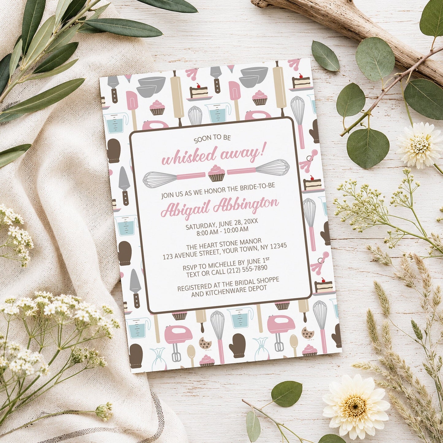 Whisked Away Pink Baking Bridal Shower Invitation shown on a light wooden surface with spring and summer plants.