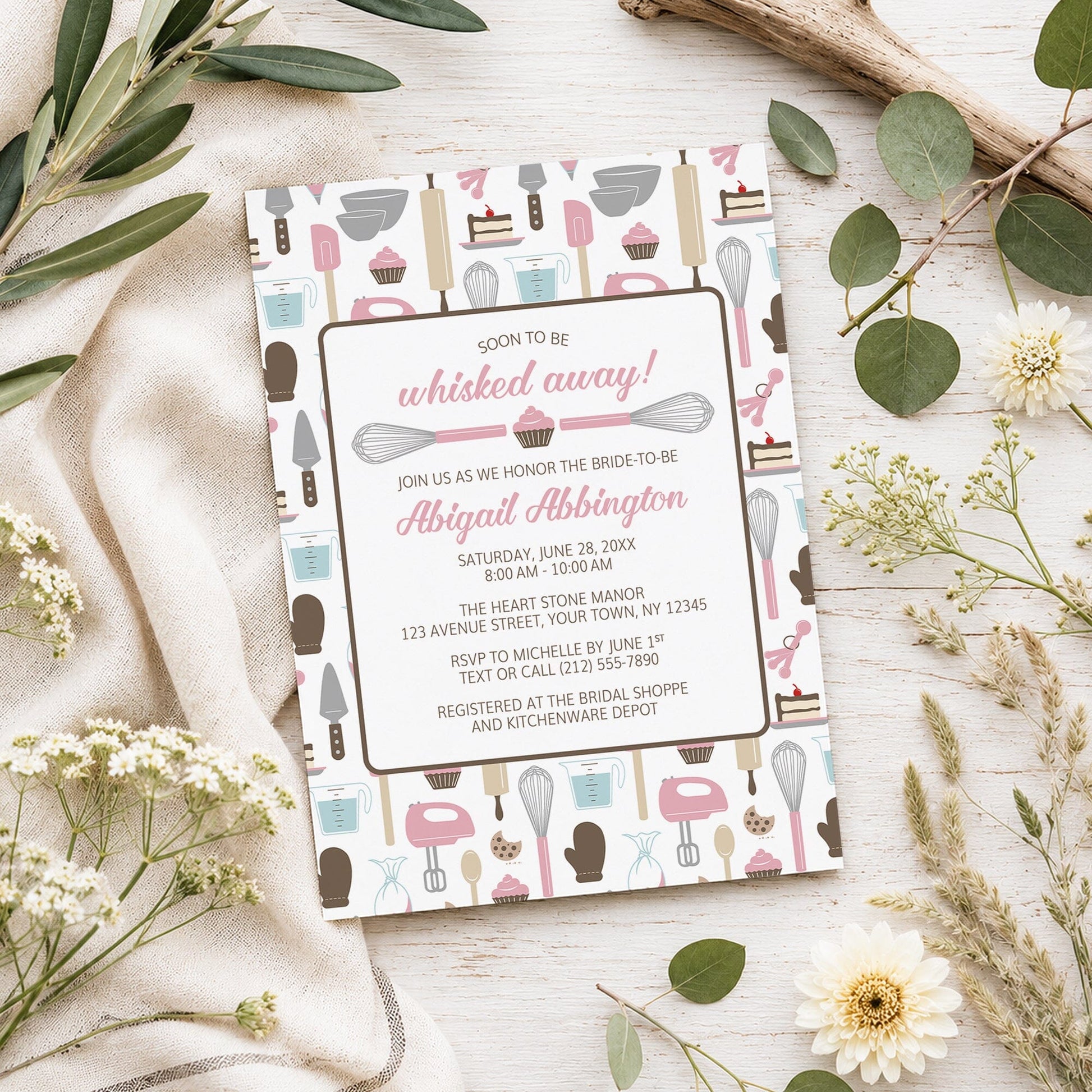 Whisked Away Pink Baking Bridal Shower Invitation shown on a light wooden surface with spring and summer plants.