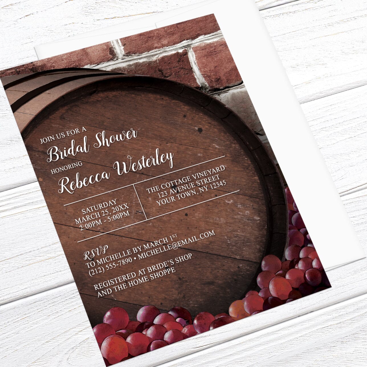 Bridal shower invitation with wooden barrel and grapes design, shown with a white envelope, on a wooden surface at an angle