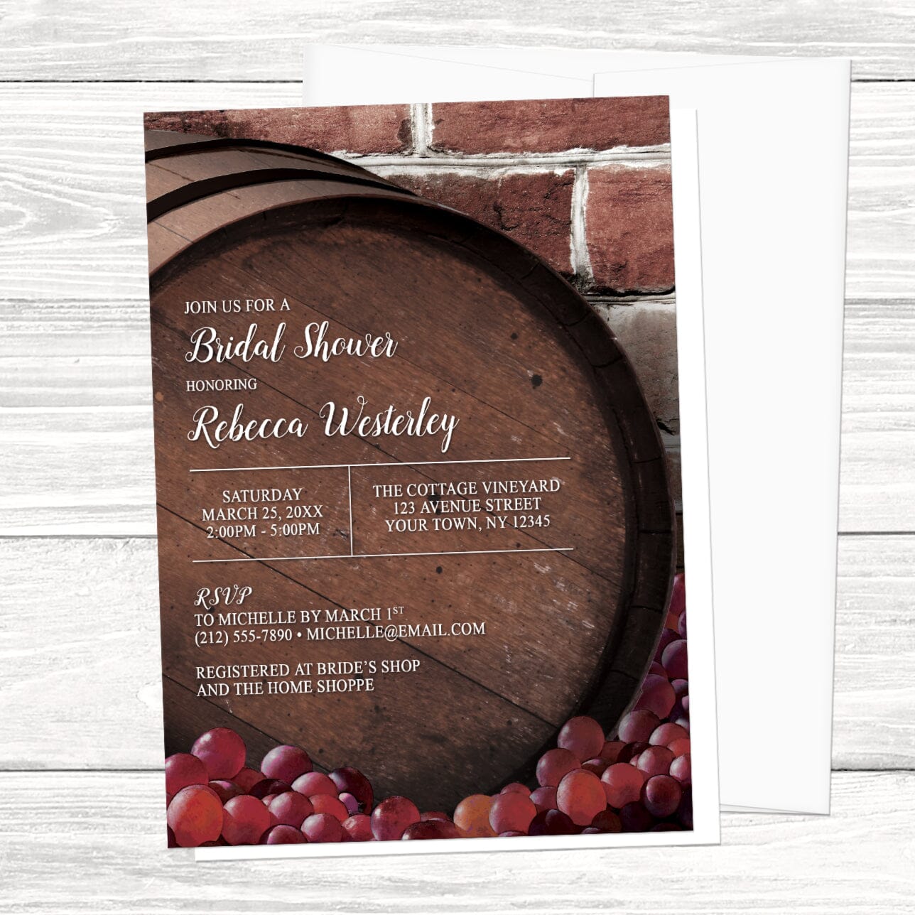 Bridal shower invitation with wooden barrel and grapes design, shown with a white envelope, on a wooden surface