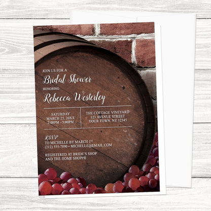Bridal shower invitation with wooden barrel and grapes design, shown with a white envelope, on a wooden surface