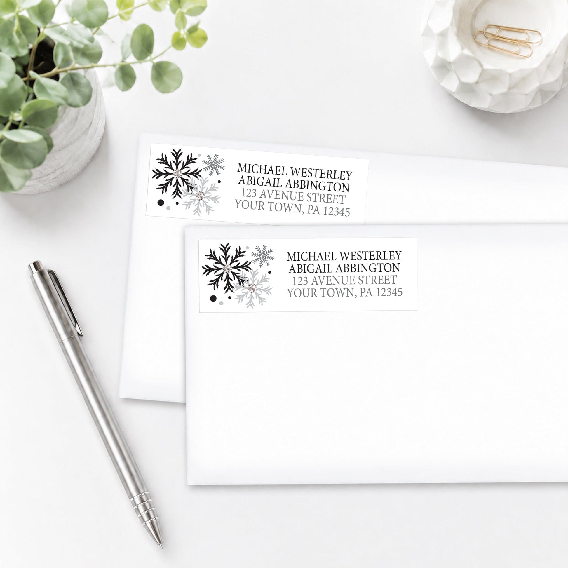 Winter Black Silver Snowflake Address Labels, shown on white envelopes, on a white surface with a pen and plant.