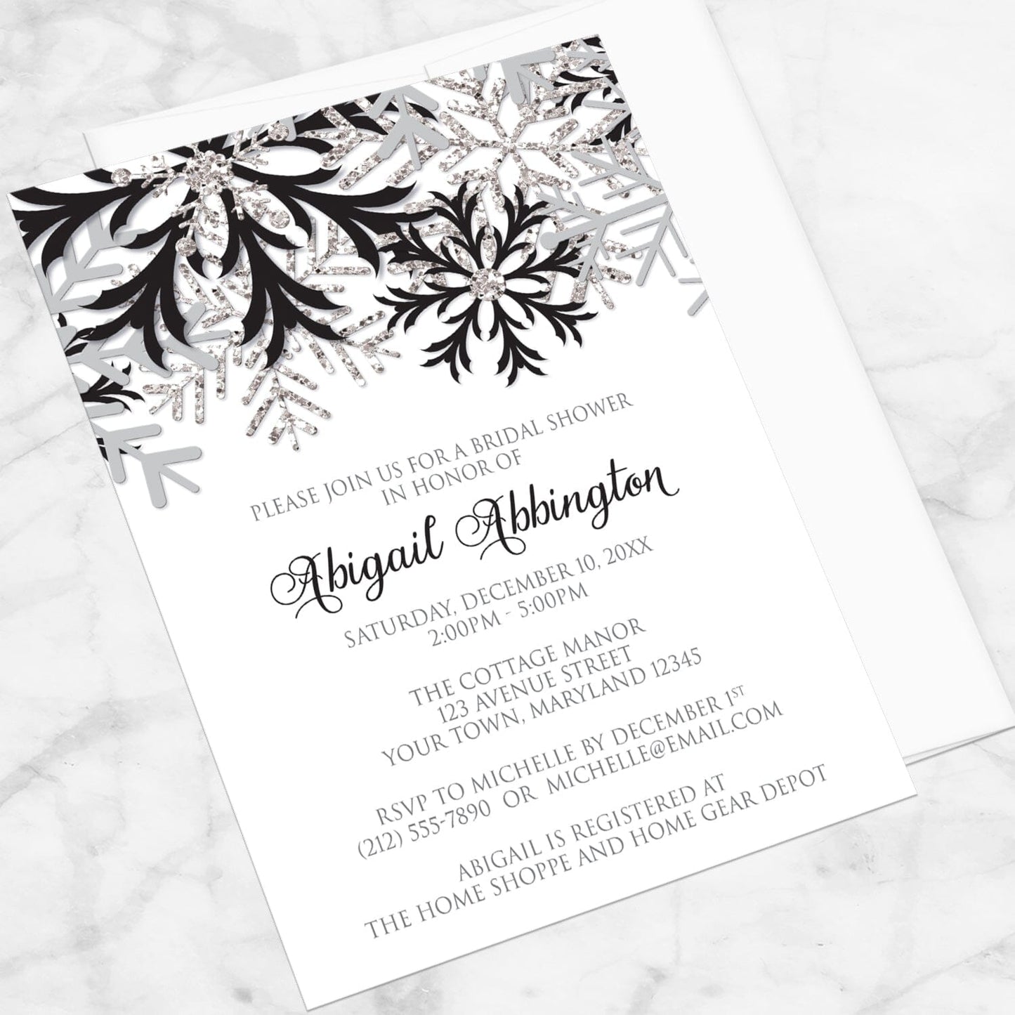 Winter Black Silver Snowflake Bridal Shower Invitation shown at an angle on a marble surface with a white envelope.