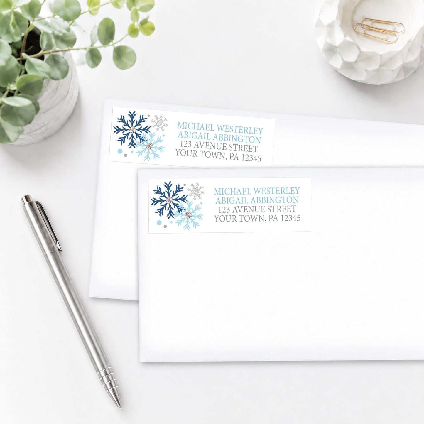 Winter Blue Silver Snowflake Address Labels shown on envelopes on a white surface with a plant and pen.