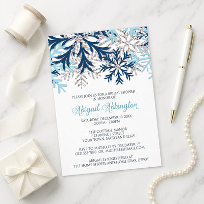 Winter Blue Silver Snowflake Bridal Shower Invitation shown on a marble surface with a white gift box, pen, ribbon, and pearls.