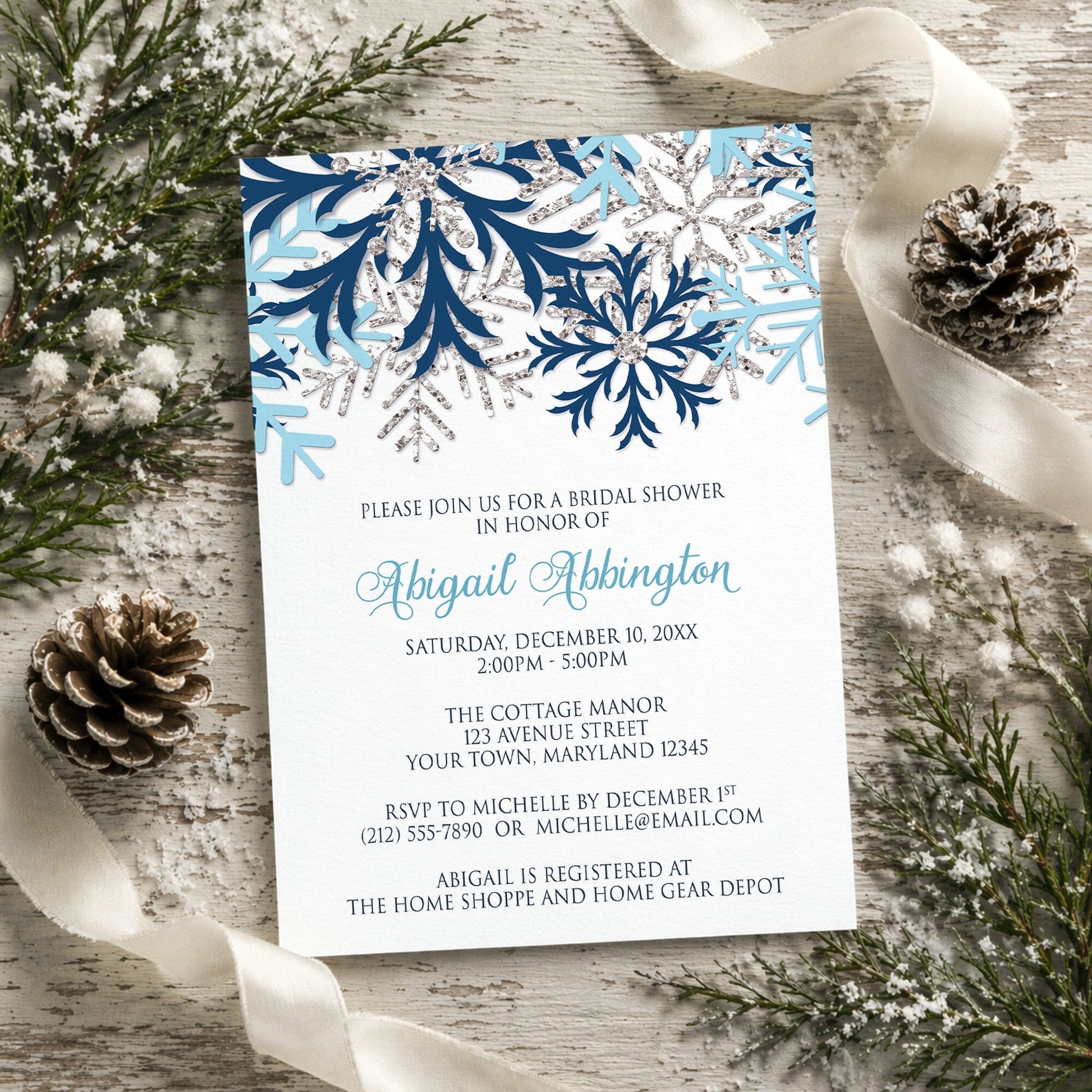 Winter Blue Silver Snowflake Bridal Shower Invitation shown on a rustic wooden surface with winter greenery, pine cones, and ribbon.
