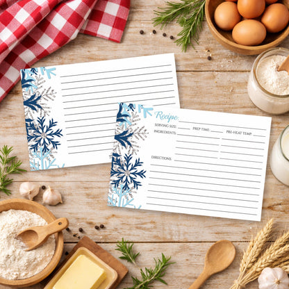 Two recipe cards with a snowflake design in blue and silver, shown on a wooden surface with cooking ingredients.