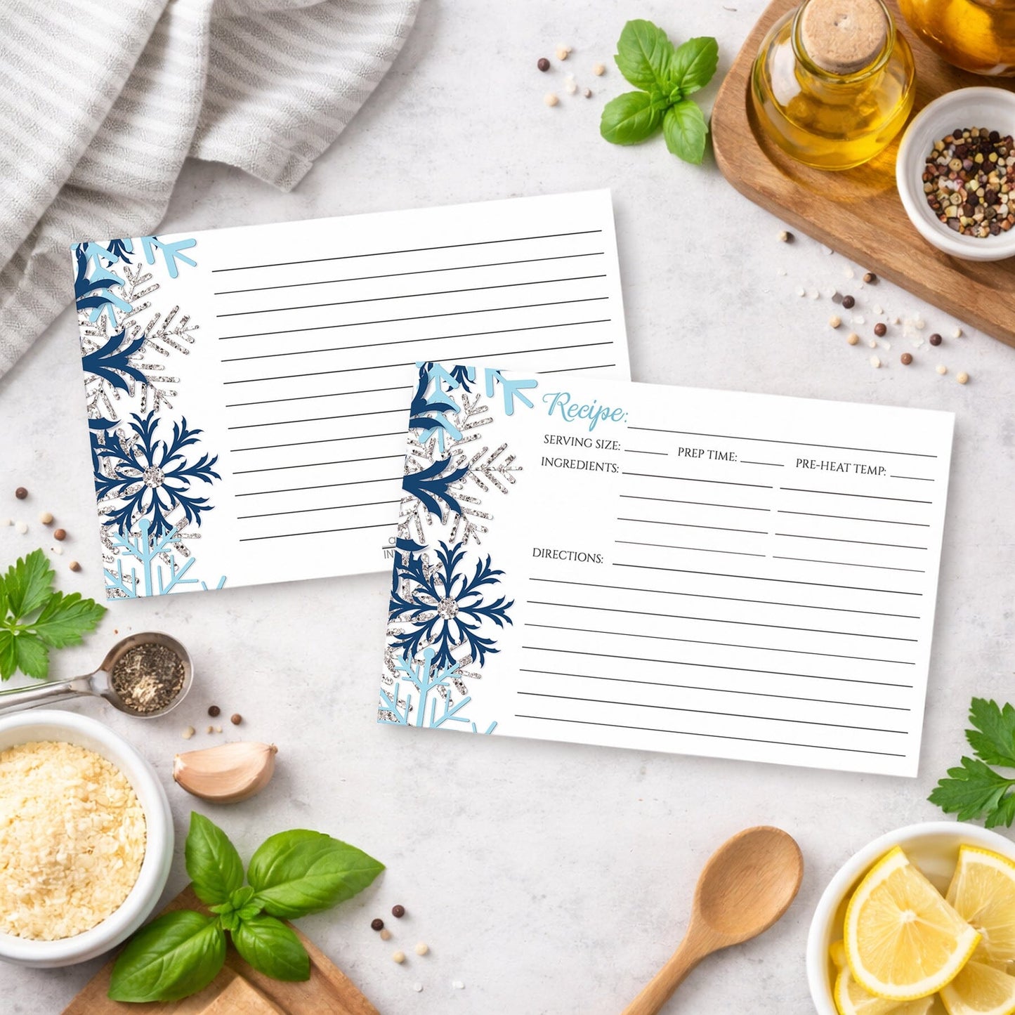 Two recipe cards with a snowflake design in blue and silver, shown on a kitchen counter with ingredients.