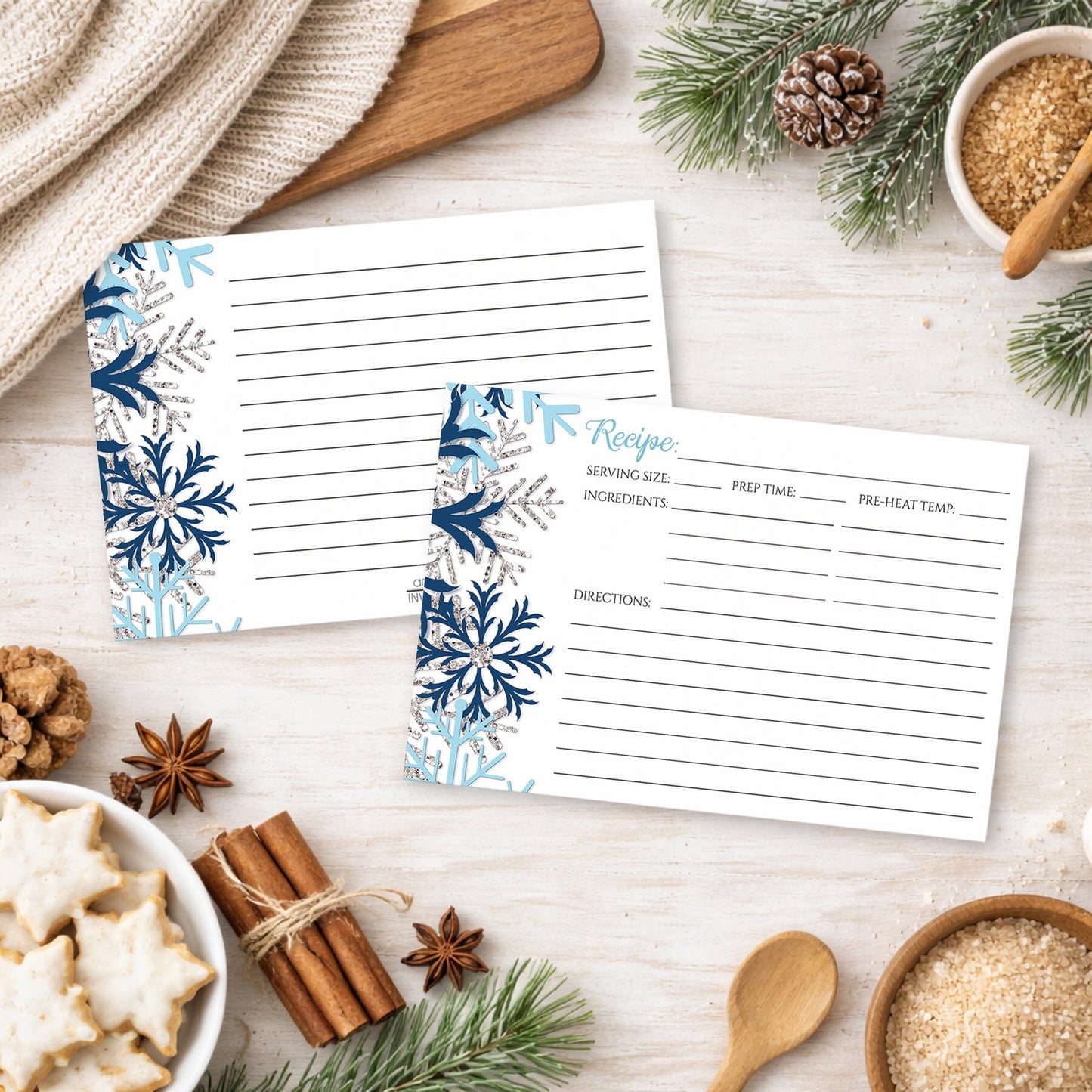 Two recipe cards with a snowflake design in blue and silver, shown on a festive holiday table with cookies and spices.