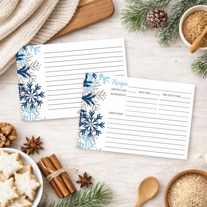 Two recipe cards with a snowflake design in blue and silver, shown on a festive holiday table with cookies and spices.