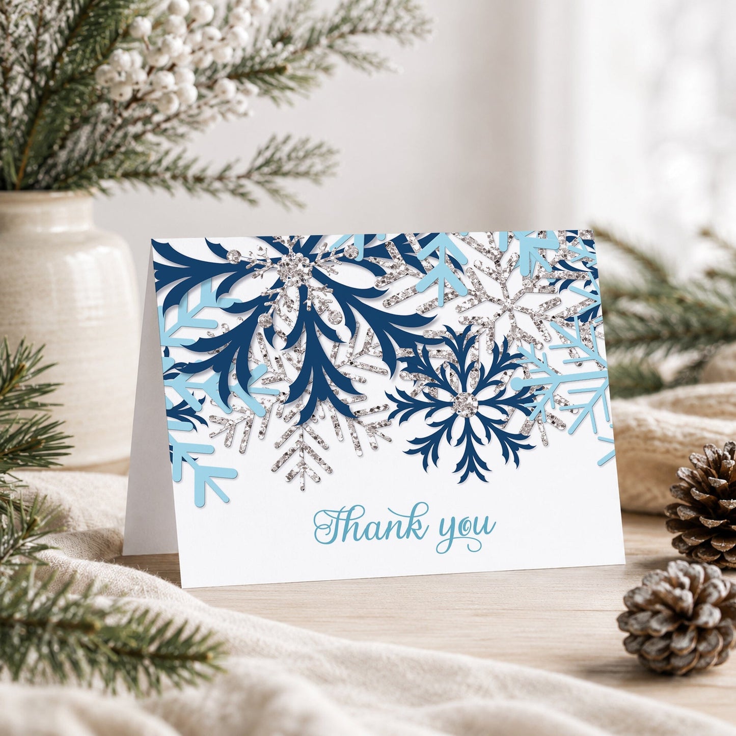 Winter Blue Silver Snowflake Thank You Card shown on a tabletop with a vase, rustic greenery, and pine cones.