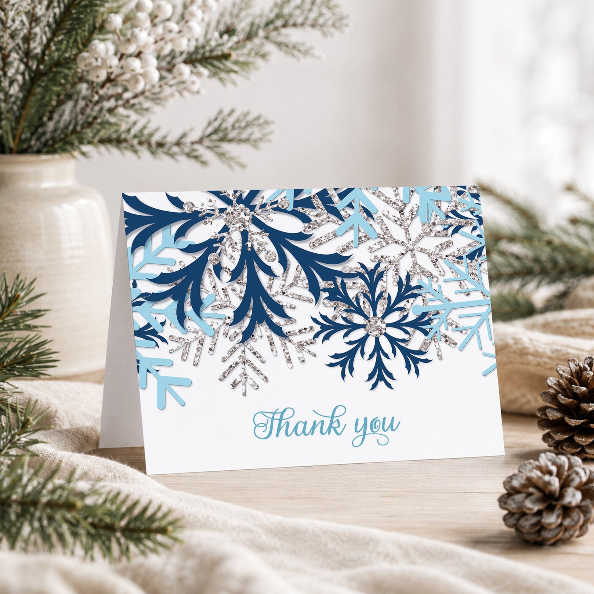 Winter Blue Silver Snowflake Thank You Card shown on a tabletop with a vase, rustic greenery, and pine cones.