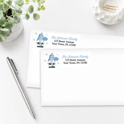 Two Winter Gnome Address Labels with a blue gnome design, shown on white envelopes, on a white surface with a pen and plant.