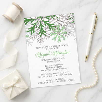 Winter Green Silver Snowflake Bridal Shower Invitation shown on a marble surface with a white gift box, pen, ribbon, and pearls.
