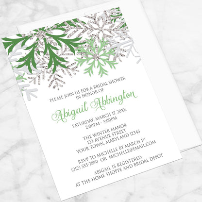 Winter Green Silver Snowflake Bridal Shower Invitation shown at an angle on a marble surface with a white envelope.
