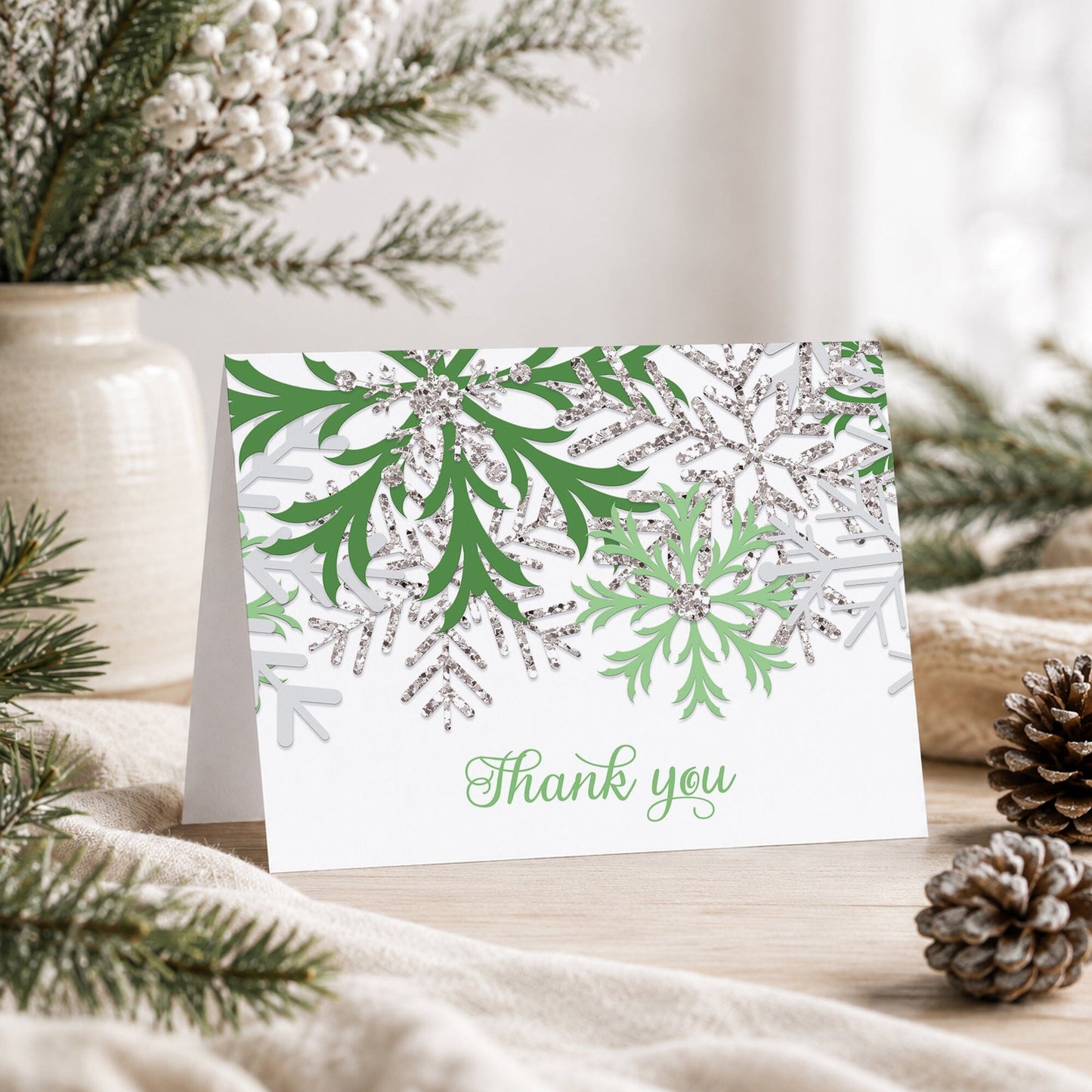Winter Green Silver Snowflake Thank You Card shown on a tabletop with a vase, winter greenery, and pine cones.