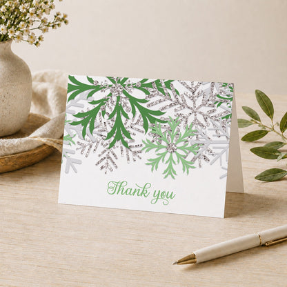 Winter Green Silver Snowflake Thank You Card shown on a desk with a vase, plants, and a pen.