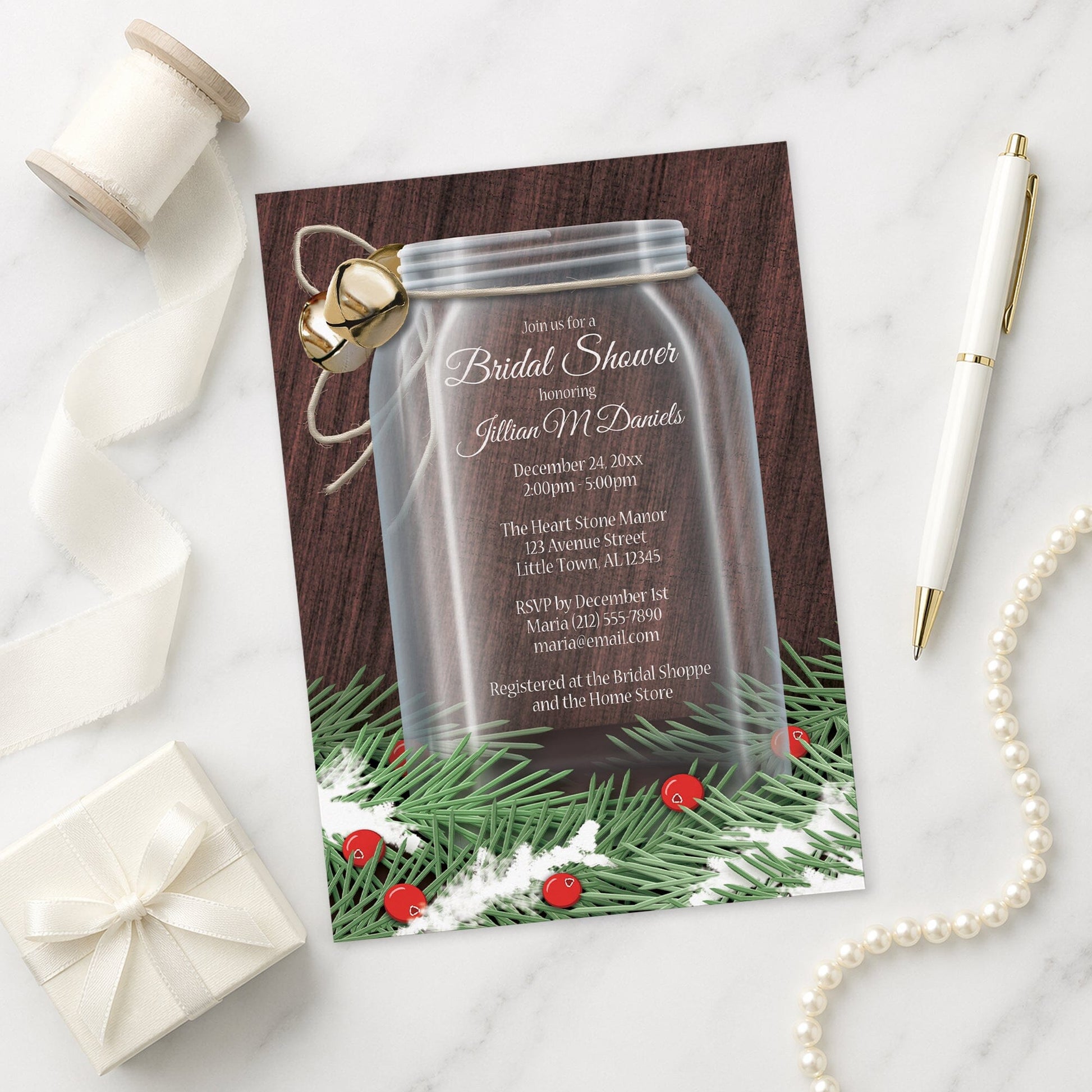 Winter Mason Jar Pine Boughs Bridal Shower Invitation shown on a marble surface with a white gift box, pen, ribbon, and pearls.