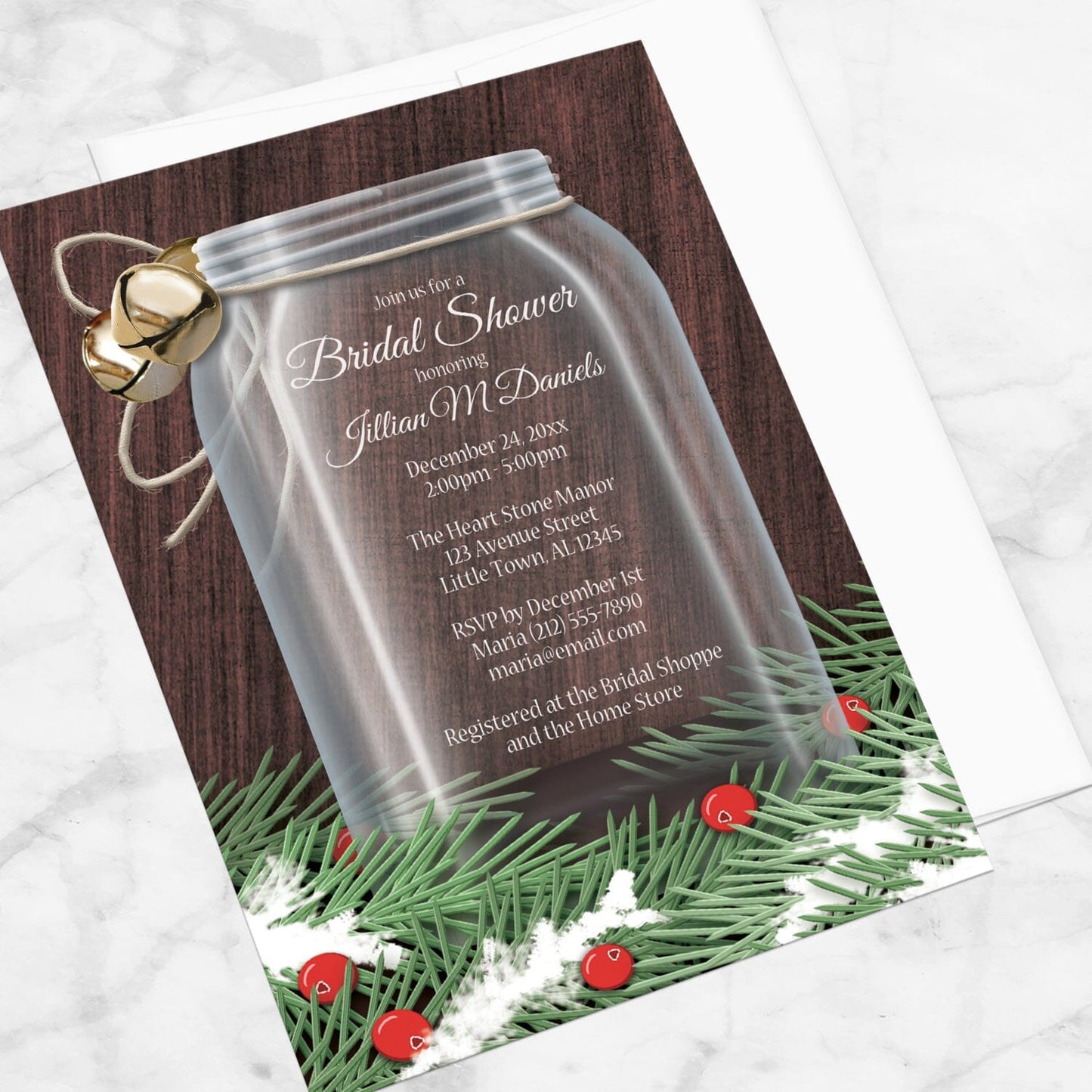 Winter Mason Jar Pine Boughs Bridal Shower Invitation shown at an angle on a marble surface with a white envelope.