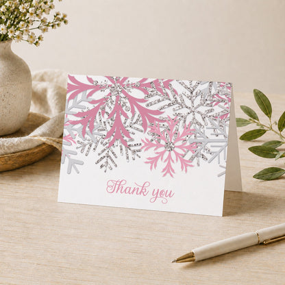 Winter Pink Silver Snowflake Thank You Card shown on a desk with a vase, plants, and a pen.
