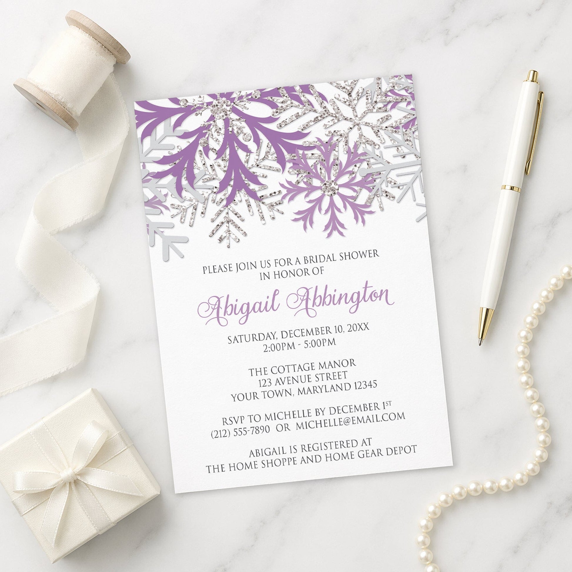 Winter Purple Silver Snowflake Bridal Shower Invitation on a marble surface with ribbon, pen, and gift box.