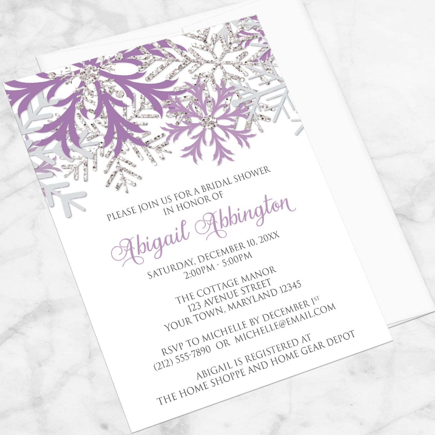 Winter Purple Silver Snowflake Bridal Shower Invitation shown at an angle on a marble surface with a white envelope.