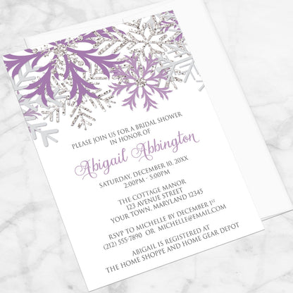 Winter Purple Silver Snowflake Bridal Shower Invitation shown at an angle on a marble surface with a white envelope.
