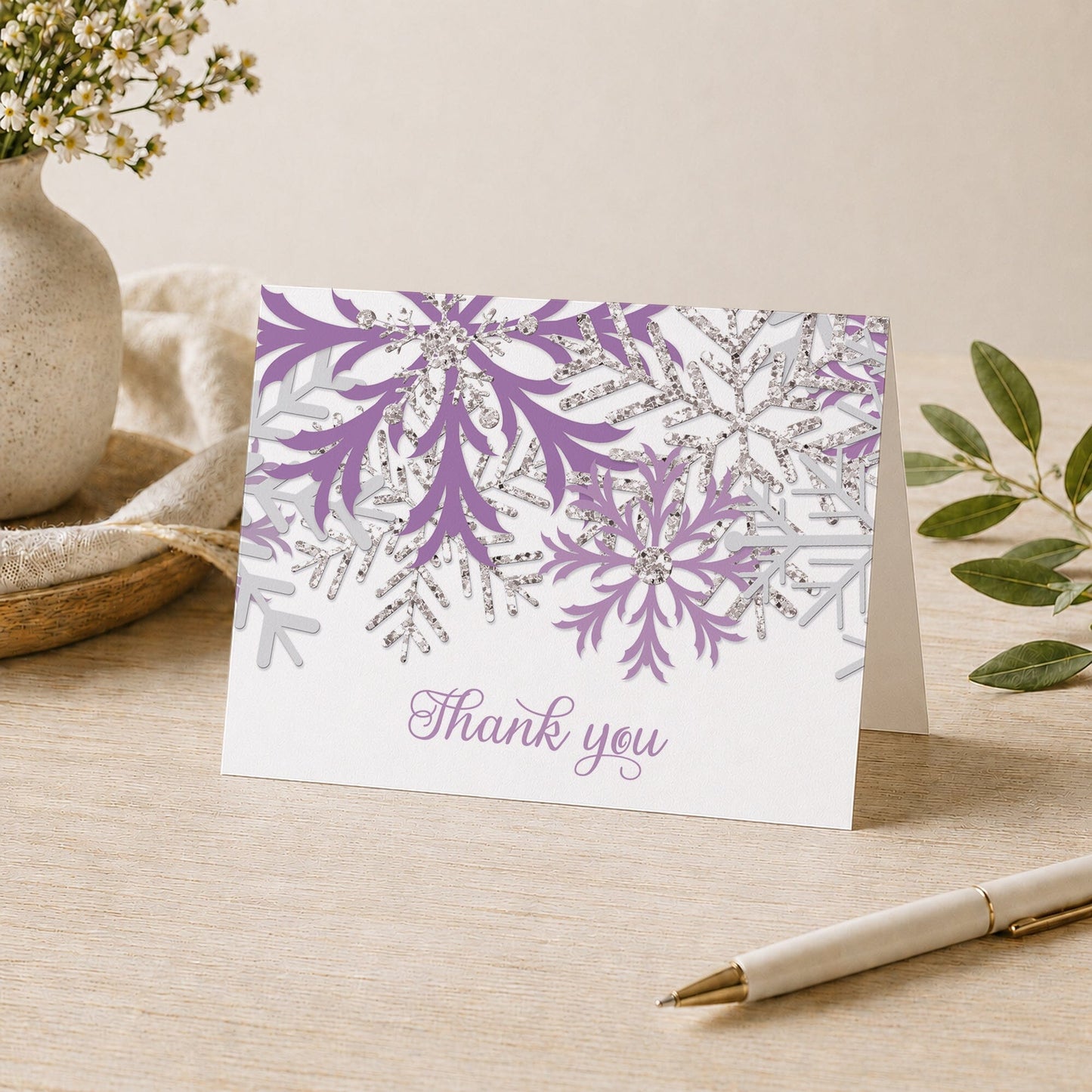 Winter Purple Silver Snowflake Thank You Card shown on a desk with a vase, plants, and a pen.