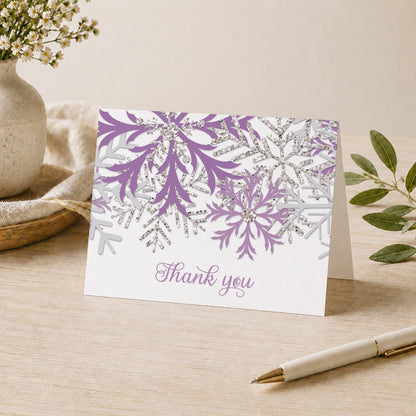 Winter Purple Silver Snowflake Thank You Card shown on a desk with a vase, plants, and a pen.