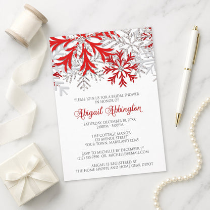 Winter Red Silver Snowflake Bridal Shower Invitation on a marble surface with a white gift box, pen, and pearls.