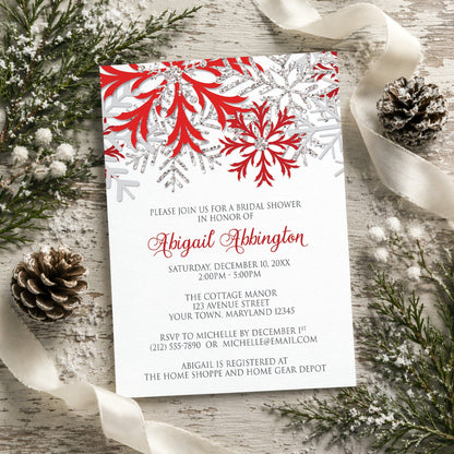 Winter Red Silver Snowflake Bridal Shower Invitation on a wooden background, surrounded by winter greenery, ribbon, and pine cones.