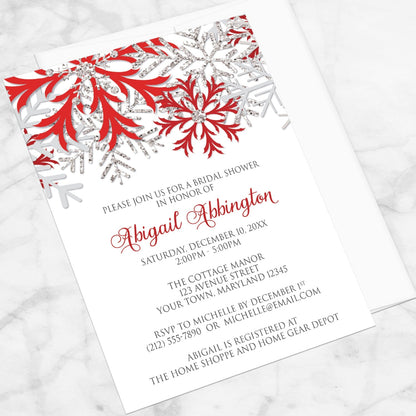 Winter Red Silver Snowflake Bridal Shower Invitation shown at an angle on a marble surface with a white envelope.