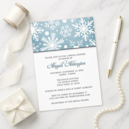 Winter Snowflake Blue Gray Bridal Shower Invitation shown on a marble surface with a white gift box, pen, ribbon, and pearls.