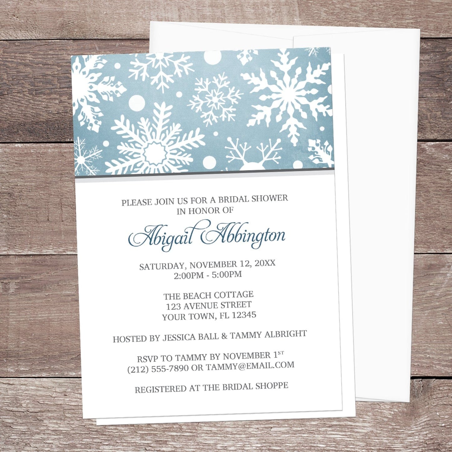 Winter Snowflake Blue Gray Bridal Shower Invitation shown on a wooden surface with a white envelope.