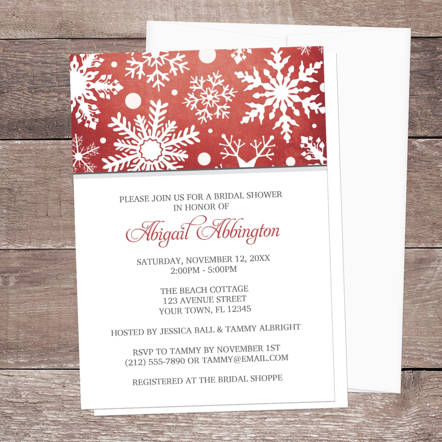 Winter Snowflake Red Gray Bridal Shower Invitation shown on a wooden surface with a white envelope.