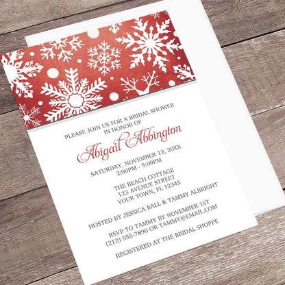 Winter Snowflake Red Gray Bridal Shower Invitation shown at an angle on a wooden surface with a white envelope.