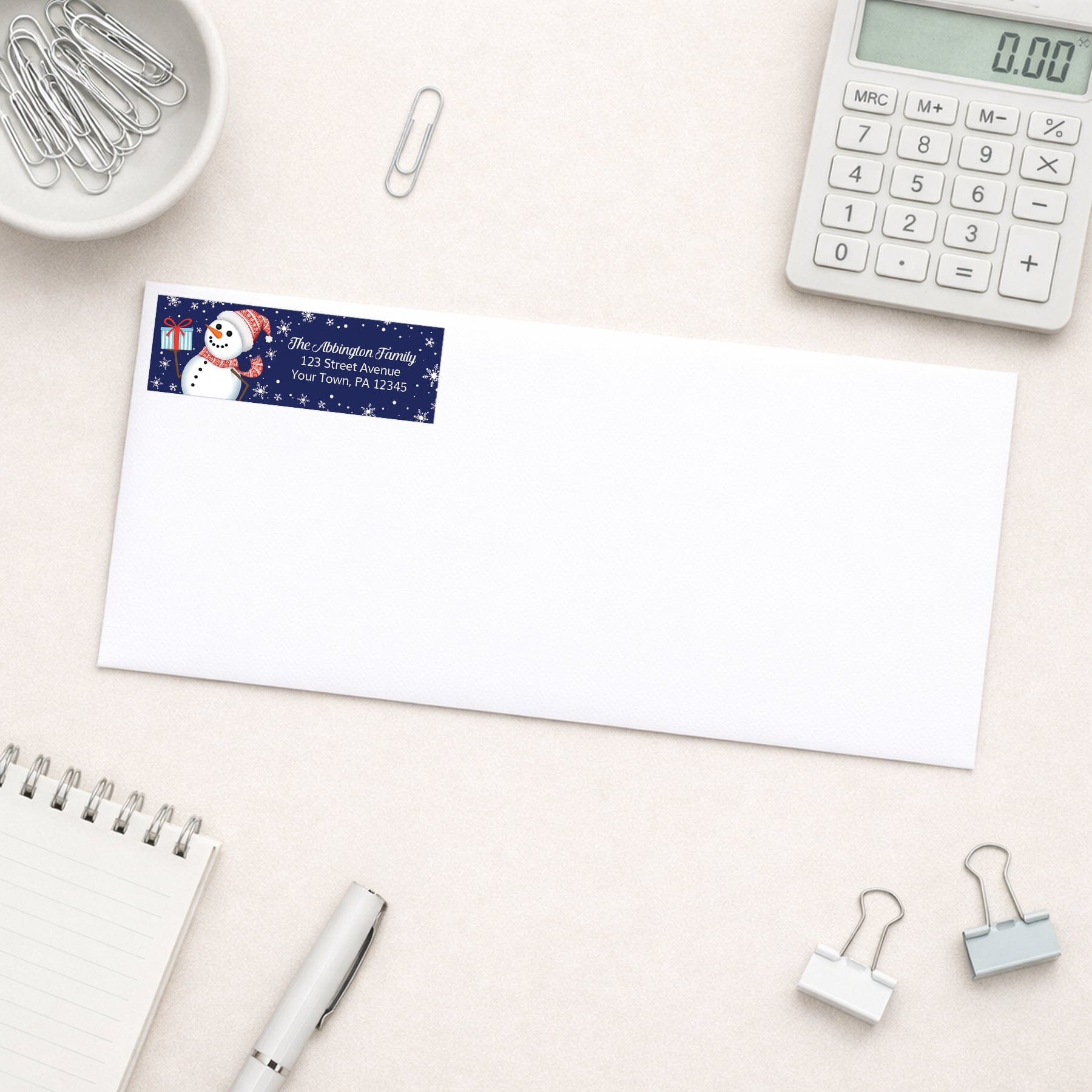 Address label with snowman design on a white envelope with office supplies around