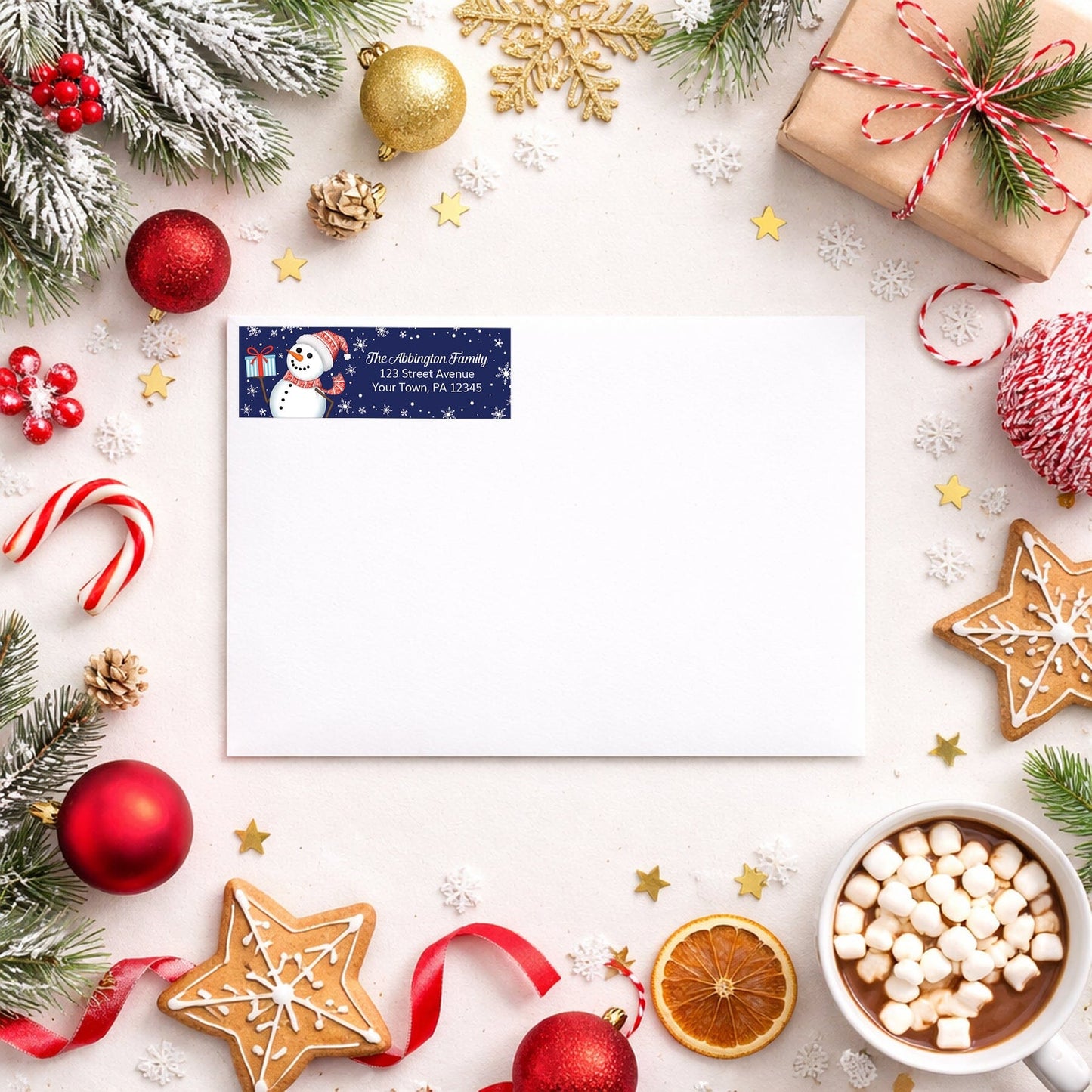 Address label with snowman design on a white envelope with winter Christmas holiday supplies around it