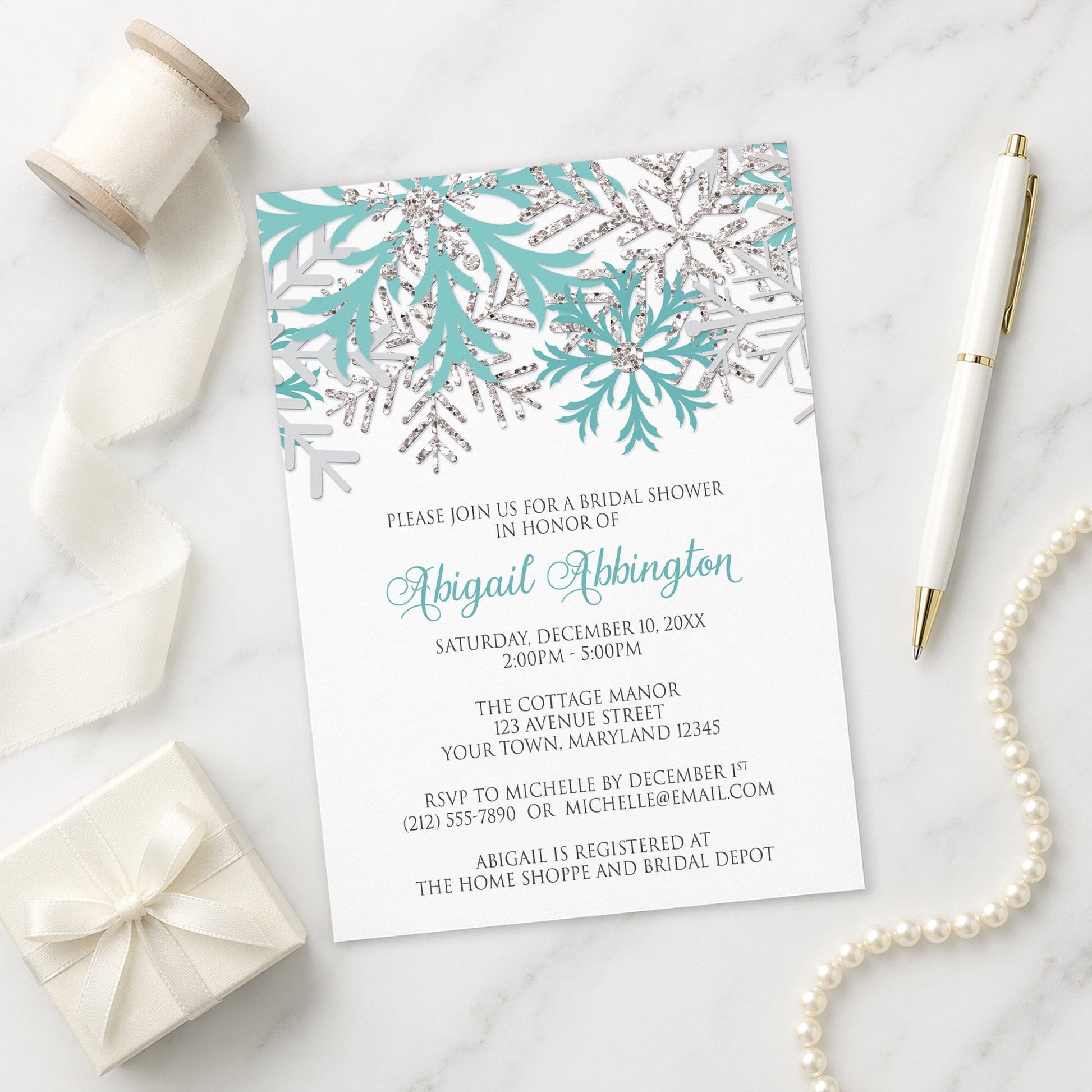 Winter Teal Silver Snowflake Bridal Shower Invitation on a marble surface with a white gift box, ribbon, pen, and pearls.
