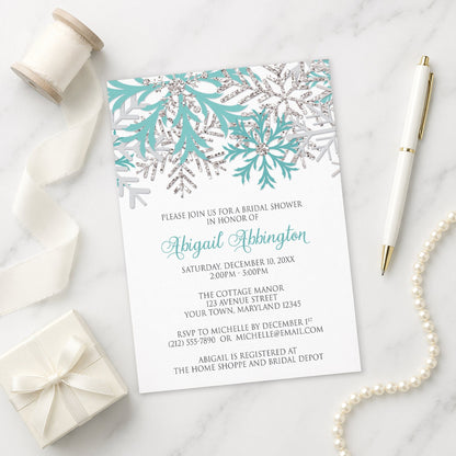 Winter Teal Silver Snowflake Bridal Shower Invitation on a marble surface with a white gift box, ribbon, pen, and pearls.