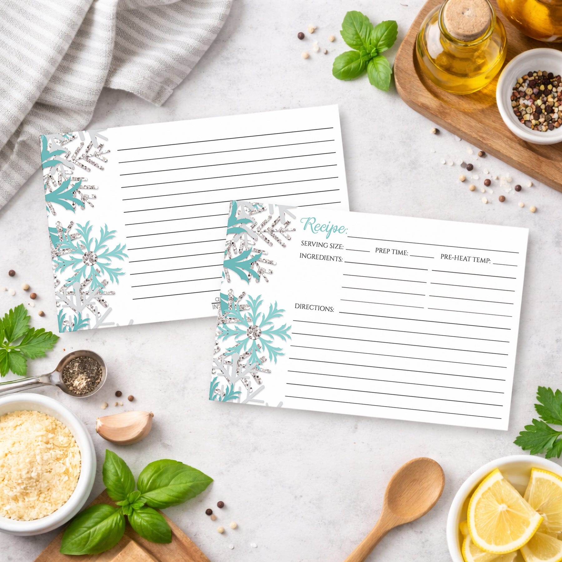Two Winter Teal Silver Snowflake Recipe Cards on a kitchen counter with ingredients.
