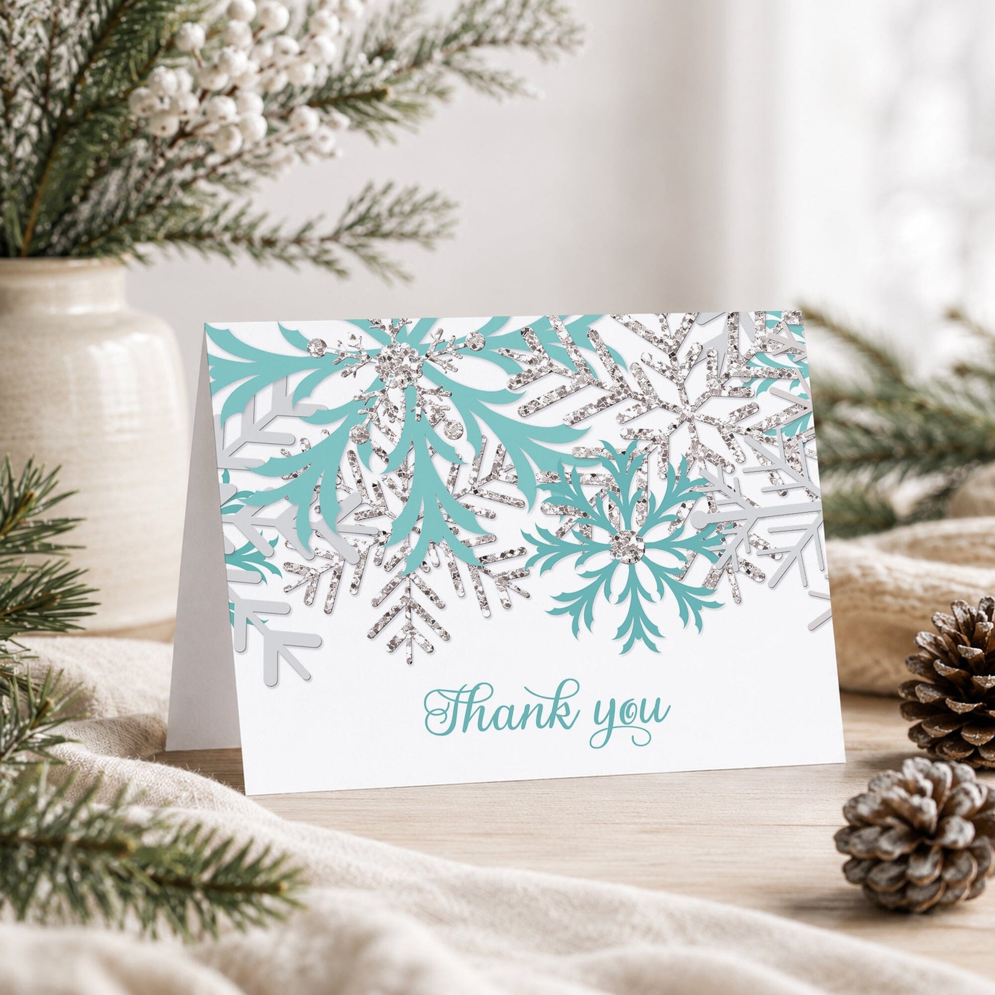 Winter Teal Silver Snowflake Thank You Card shown on a tabletop with a vase, winter greenery, and pine cones.