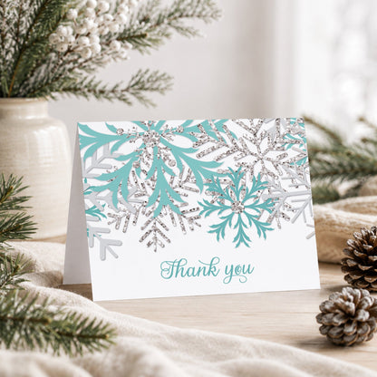 Winter Teal Silver Snowflake Thank You Card shown on a tabletop with a vase, winter greenery, and pine cones.
