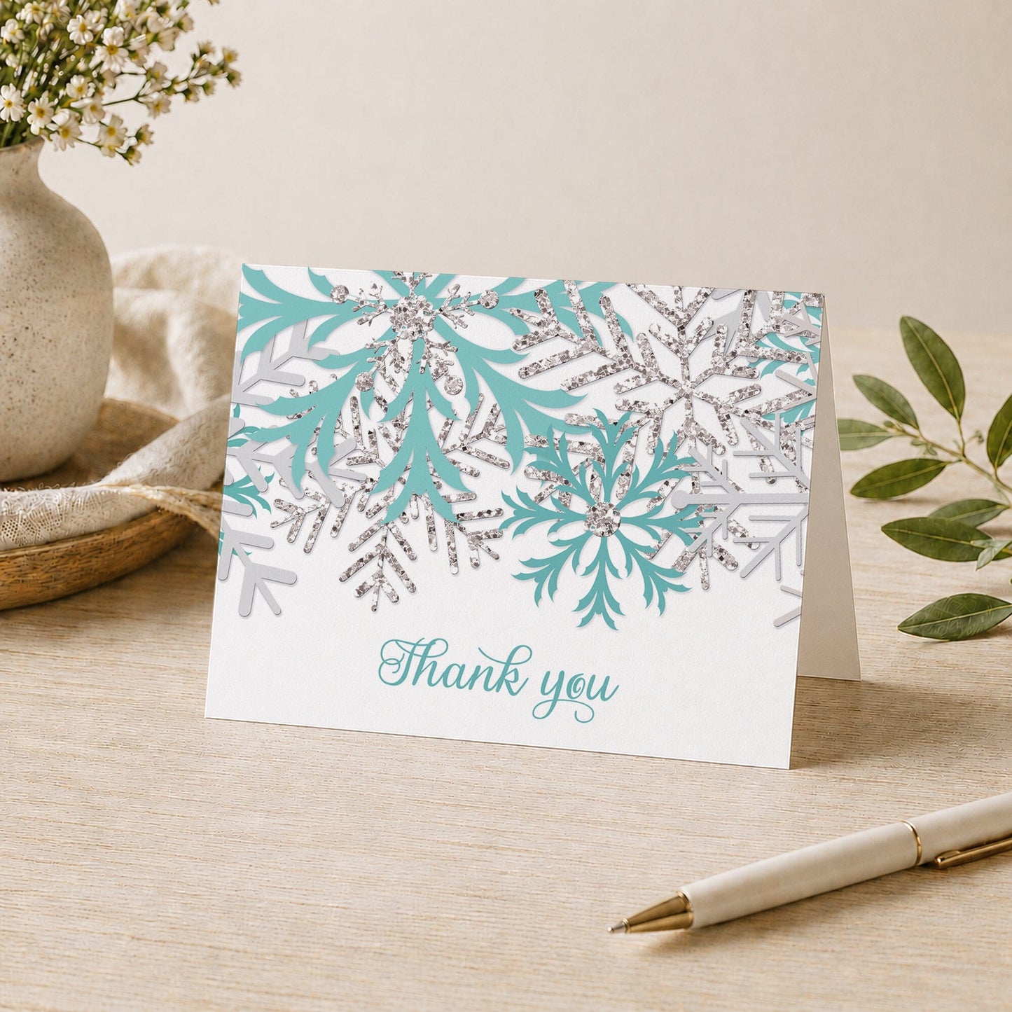 Winter Teal Silver Snowflake Thank You Card on a desk with a vase, plants, and a pen.